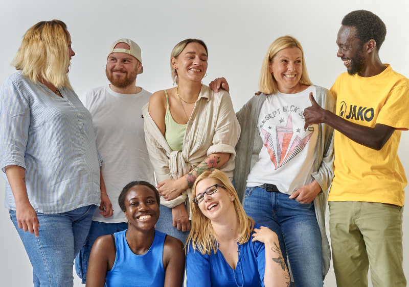 Ein Gruppenbild mit 7 Personen, die vor einer weißen Wand stehen und Spaß habe