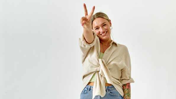 Eine Frau zeigt das Peace-Zeichen und lacht in die Kamera